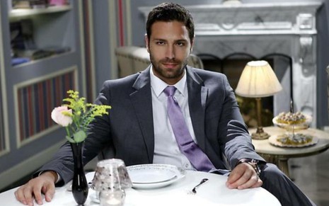 João Gabriel Vasconcellos aparece sentado à mesa em cena como Armando em Chiquititas (2013)