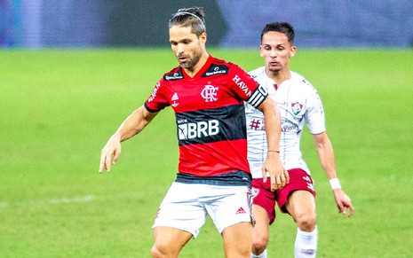 Diego com a camisa vermelha e preta do Flamengo olhando para baixo com um adversário atrás