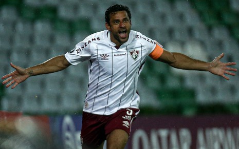 Fred com uniforme branco com linhas vermelhas do Fluminense corre com braços abertos comemorando um gol