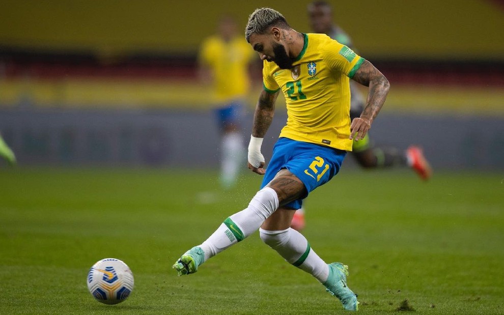 Gabigol com meião branco, calção azul e camiseta amarela do Brasil chuta a bola com a perna esquerda
