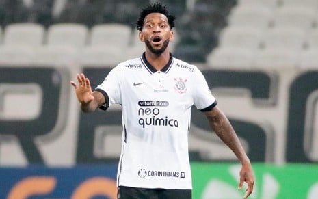 Gil com a camisa branca de calção preto do Corinthians com o braço direito levantado e expressão de espanto