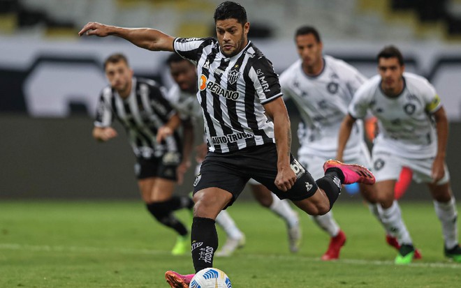 Hulk com a camisa branca e preta do Atlético-MG em movimento de chute da bola com a perna esquerda