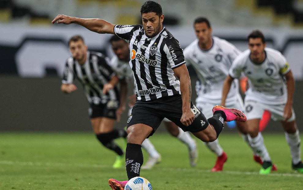 Hulk com a camisa branca e preta do Atlético-MG em movimento de chute da bola com a perna esquerda