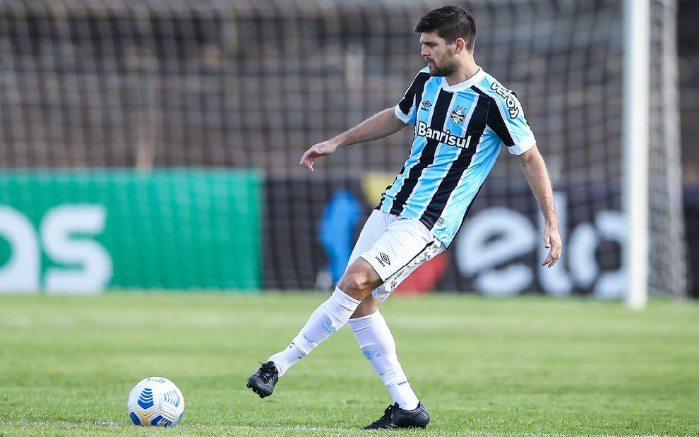 Kannemann com meião branco, calção branco e camisa azul, preta e branca do Grêmio faz passe lateral para o lado esquerdo