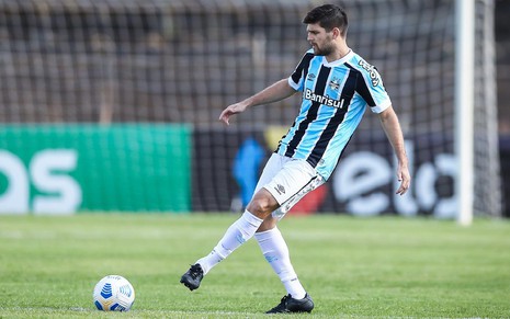 Kannemann com meião branco, calção branco e camisa azul, preta e branca do Grêmio faz passe lateral para o lado esquerdo