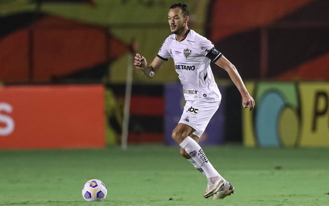 Réver com calção branco e camisa branca do Atlético-MG olha para a bola no chão em sua frente no lado esquerdo