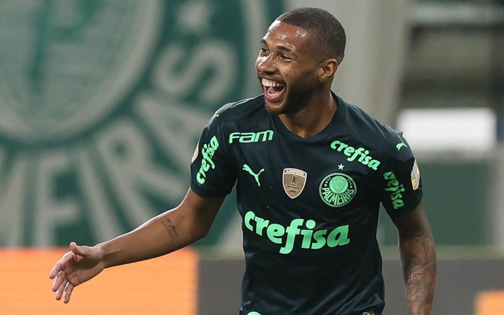 Wesley em campo com a camisa verde do Palmeiras sorrindo e com o braço direito aberto