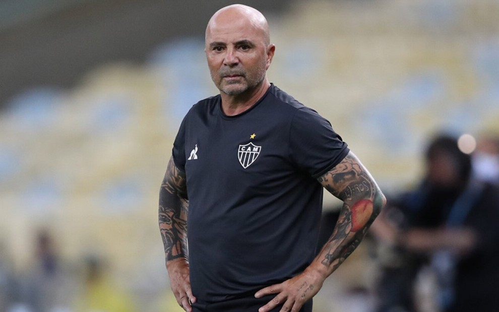 O técnico do Atlético-MG, Jorge Sampaoli na lateral de com a mãos no quadril, ele veste calça preta e camisa preta com escudo do time