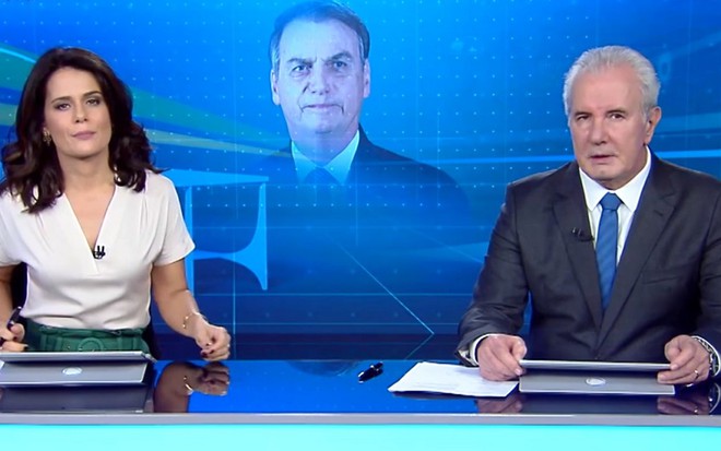 Adriana Araújo e Celso Freitas na bancada do Jornal da Record, com uma arte do presidente Jair Bolsonaro ao fundo