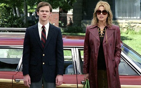 Joseph Cross e Annette Bening em pé, lado a lado, em frente a um carro