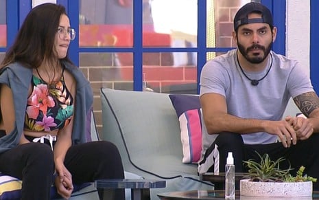 Juliette Freire e Rodolffo Matthaus, de boné, conversam sentados na área externa da casa do BBB21