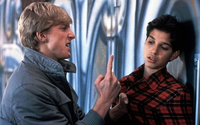 William Zabka empurra Ralph Macchio na parede em cena do filme Karatê Kid