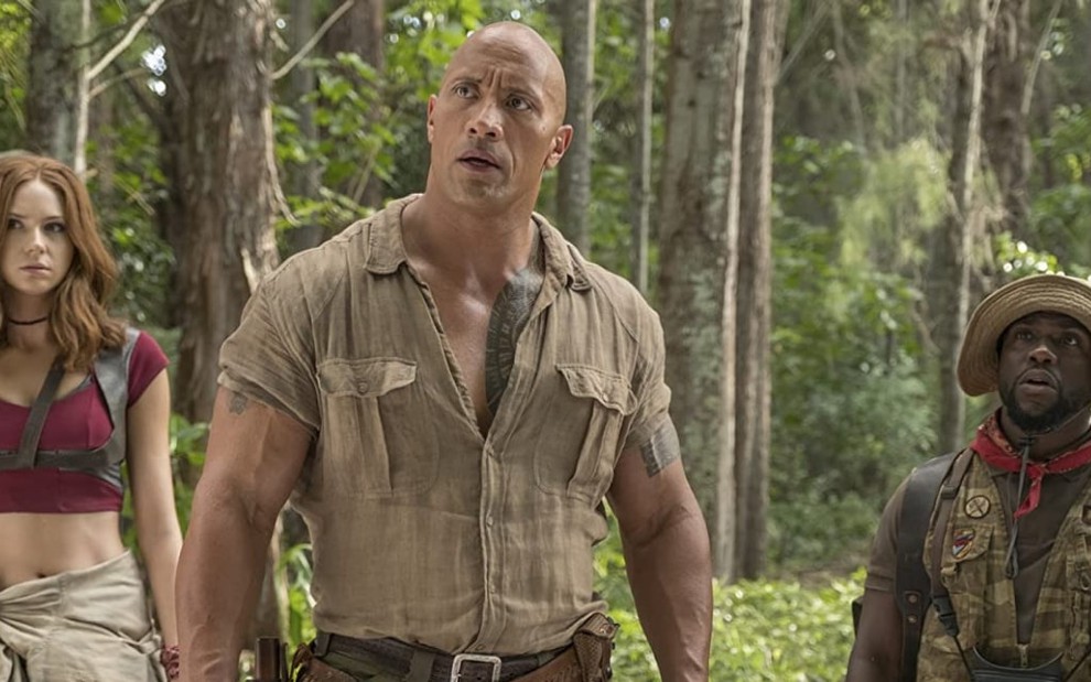 Karen Gillan, Dwayne Johnson e Kevin Hart com expressões confusas em uma floresta em cena de Jumanji - Bem-Vindo à Selva