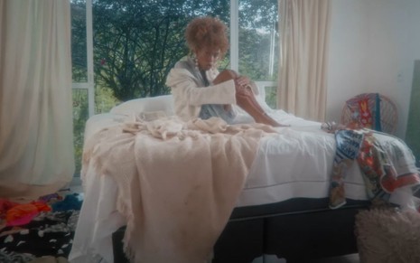Imagem de Karol Conká sentada em uma cama em um quarto bagunçado no clipe de Dilúvio