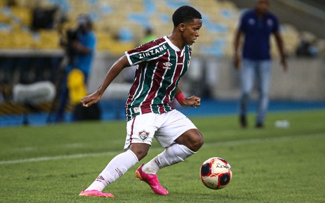 Kayky com camisa vermelha, verde e branca e calção branco do Fluminense dominando a bola