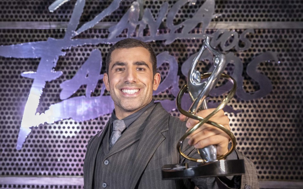 Kaysar Dadour segura um troféu e sorri na frente do letreiro de um reality show 