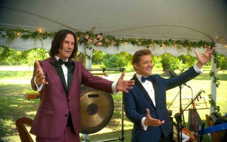 Keanu Reeves e Alex Winter com roupas de gala, em cima de um palco, realizando uma apresentação