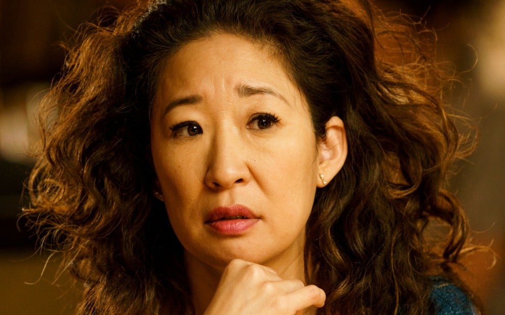 Com um penteado avolumado, Sandra Oh coloca a mão direita no queixo em cena da série Killing Eve