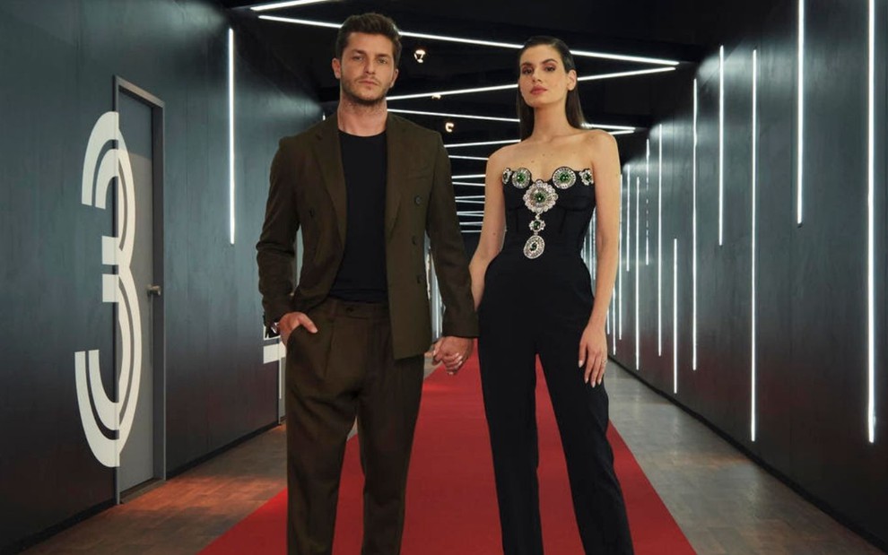 Klebber Toledo e Camila Queiroz posam de mãos dadas no corredor lado das cabines de encontro do reality show Casamento às Cegas