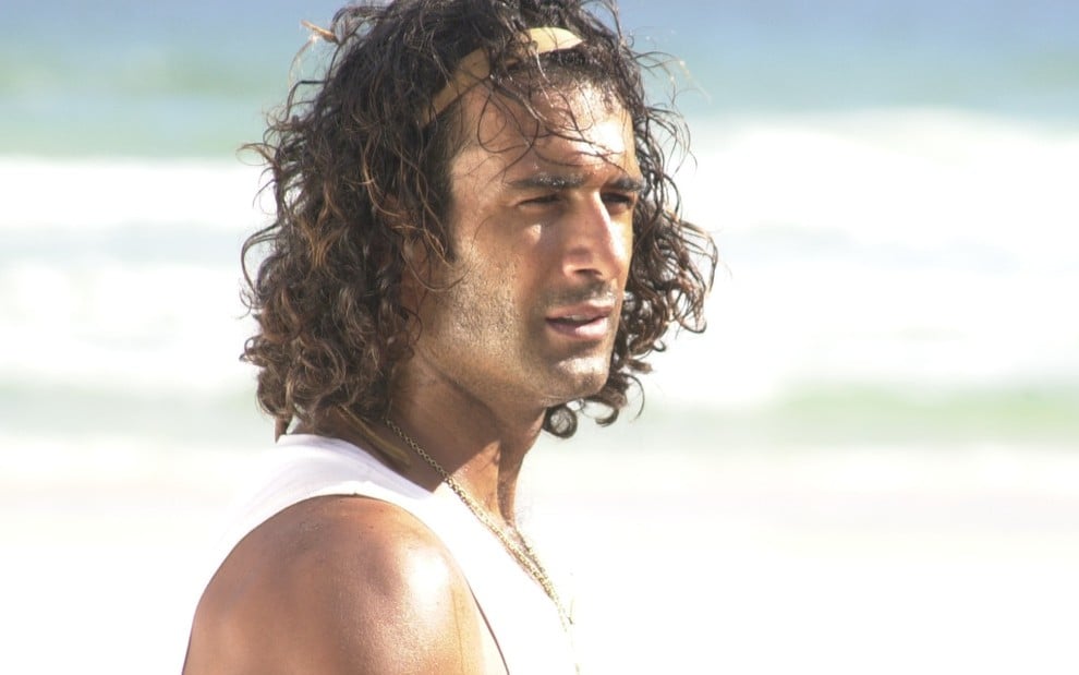 O ator Marcos Pasquim de perfil, numa praia, em cena como o personagem Esteban de Kubanacan (2003)