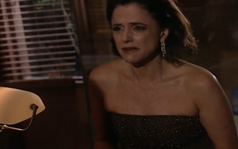 A atriz Marieta Severo com vestido preto de festa, chora na frente de um espelho em cena de Laços de Família