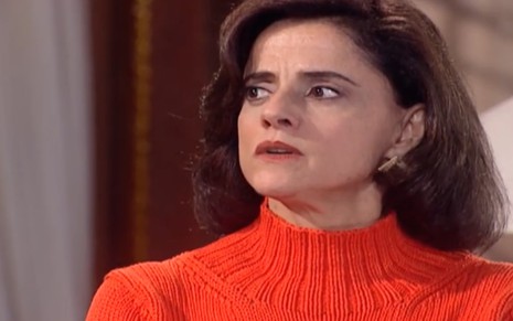 A atriz Mariera Severo de blusa de lã laranja, com expressão séria em cena como Alma em Laços de Família