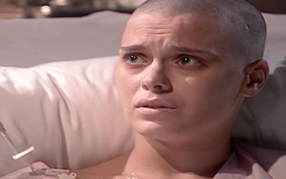 A atriz Carolina Dieckmann com expressão abatida e preocupada em cama de hospital, em cena de Laços de Família