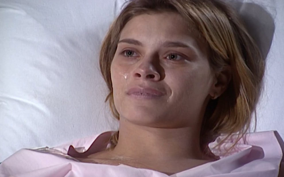 A atriz Carolina Dieckmann com expressão abatida e pálida em cama de hospital, em cena de Laços de Família