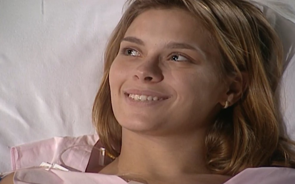 A atriz Carolina Dieckmann sorri deitada em cama de hospital em cena como Camila de Laços de Família
