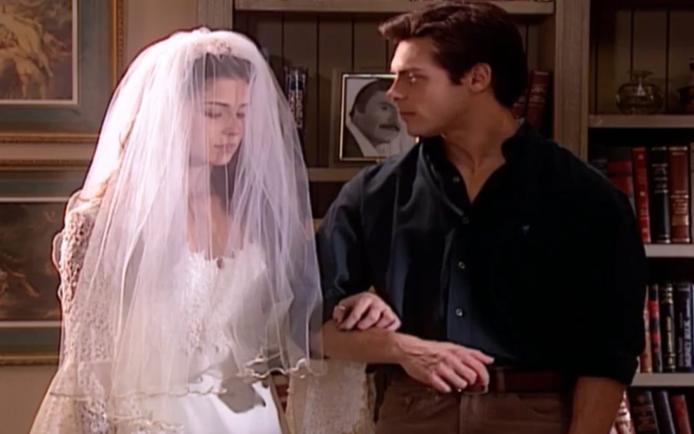 Giovanna Antonelli vestida de noiva e de braços dados com Luigi Baricelli na sala da casa da personagem Capitu