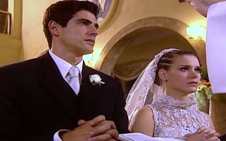 Os atores Reynaldo Gianecchini e Carolina Dieckmann vestidos de noivos e ajoelhados em frente a altar em Laços de Família