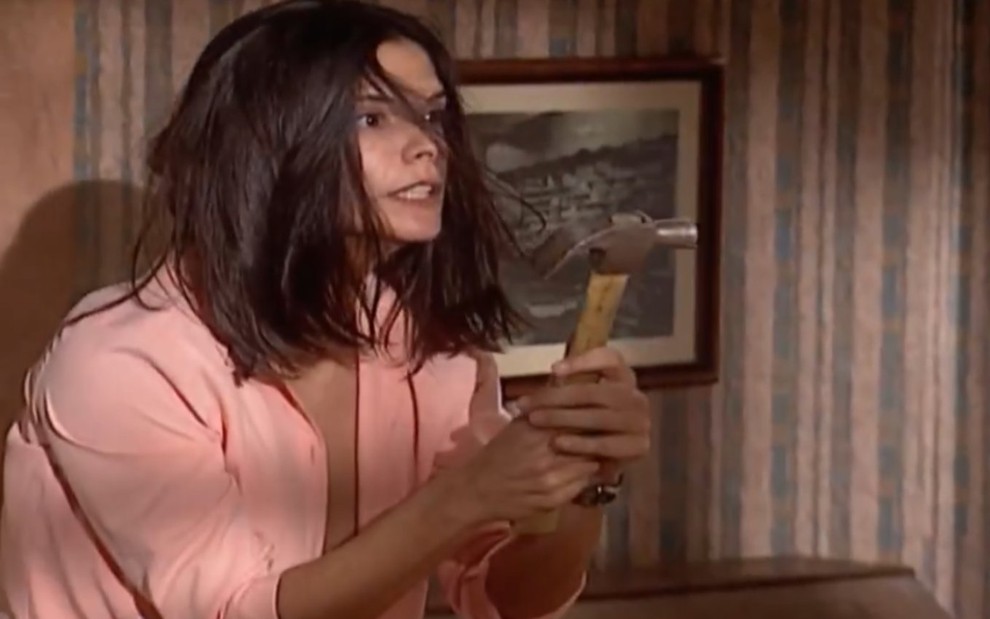 A atriz Helena Ranaldi com cabelos no rosto e martelo nas mãos em cena de Laços de Família