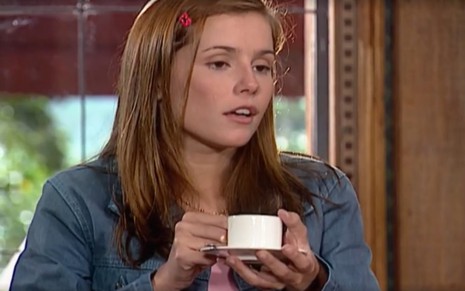 A atriz Deborah Secco com xícara e pires nas mãos e expressão de desdém em cena de Laços de Família