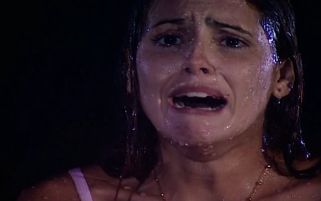 A atriz Deborah Secco com expressão de choro, toda molhada pela chuva, em cena noturna de Laços de Família