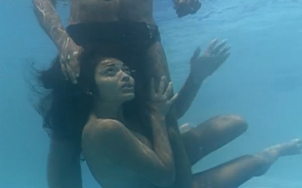 A atriz Juliana Paes seminua, debaixo d'água numa piscina, entre as pernas de Alexandre Borges e com expressão preocupada