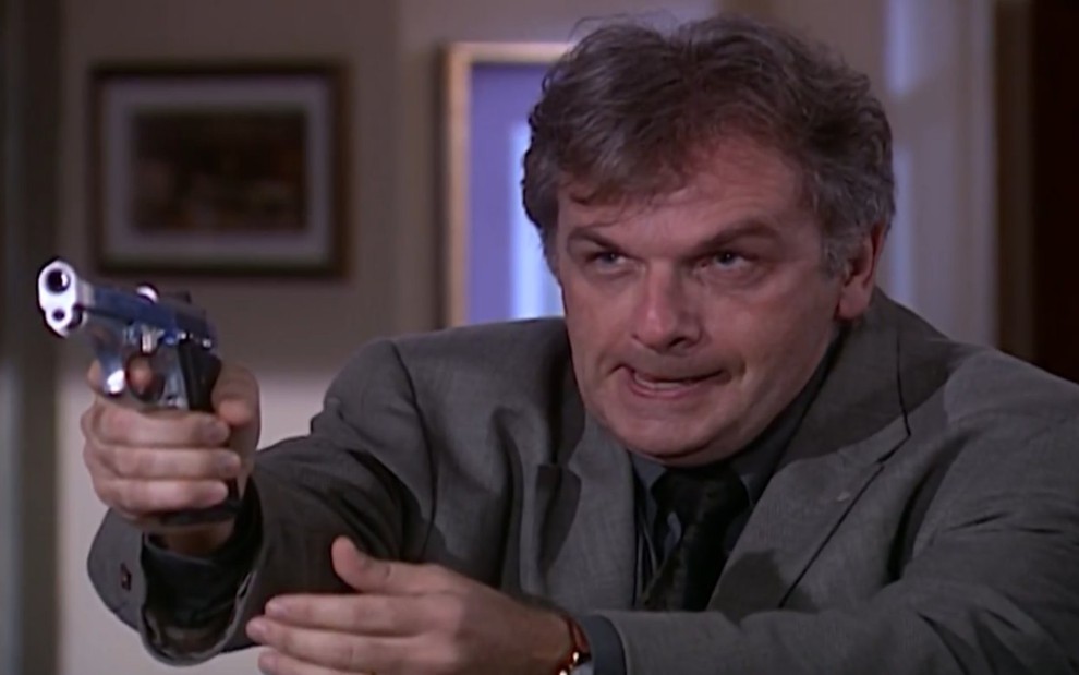 O ator Henri Pagnoncelli com expressão transtornada, segura revólver em cena de Laços de Família