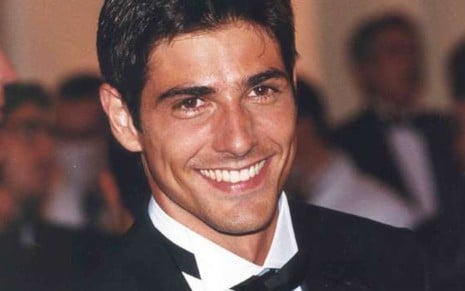 Reynaldo Gianecchini sorri de terno, camisa e gravata em cena como Edu em Laços de Família (2000)