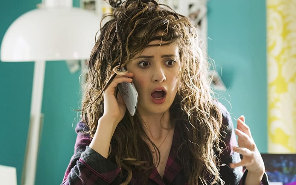 A atriz Laura Marano toda descabelada enquanto conversa no telefone e faz expressão de choque no filme Em Busca do Baile