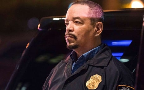 Em Law & Order: SVU, Ice-T fecha a cara ao lado de uma viatura, vestindo uniforme de polícia e esbanjando escudo de detetive no peito