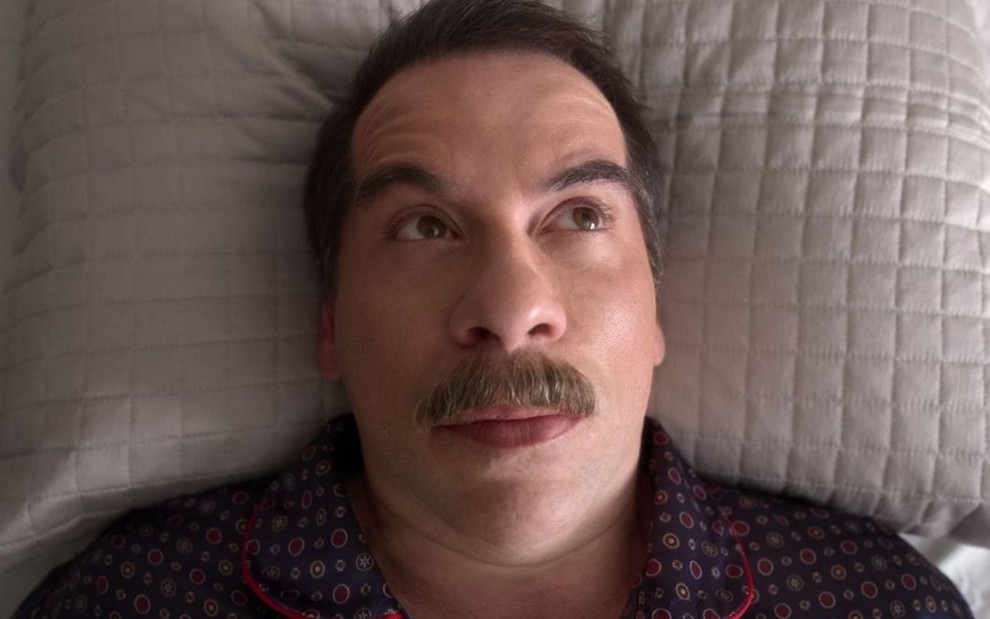 De bigode, Leandro Hassum está deitado em cena do filme Tudo Bem no Natal que Vem