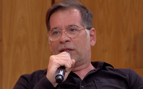 Leandro Hassum de óculos de grau e blusa preta sentado no palco do Encontro com Fátima Bernardes