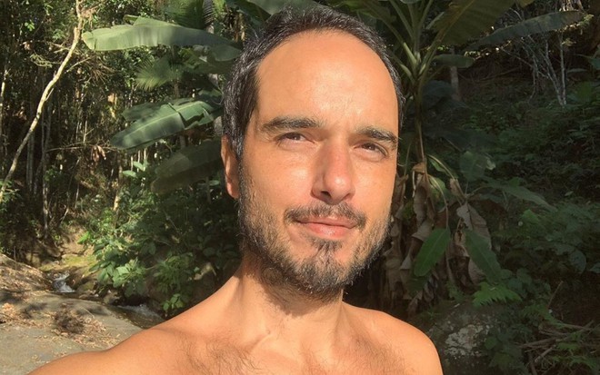 Léo Rosa sem camiseta com plantas ao fundo