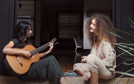 Ana Caetano toca violão sentada no chão e Vitória Falcão canta; Anavitória