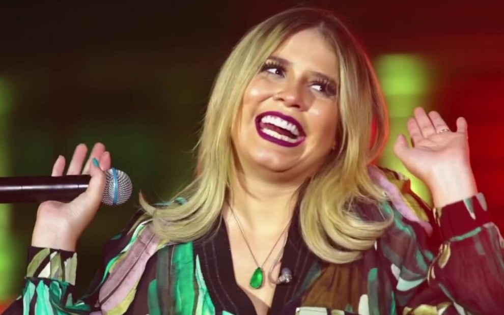 Marília Mendonça segura o microfone e sorri durante show, que está disponível no YouTube