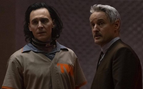 Loki (Tom Hiddleston) à esquerda com roupa de prisioneiro e estranho colar, e Mobius (Owen Wilson) à direita com paletó