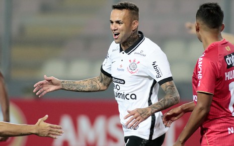 Luan com a camisa branca do Corinthians corre animado e é observado por um adversário de camisa vermelha