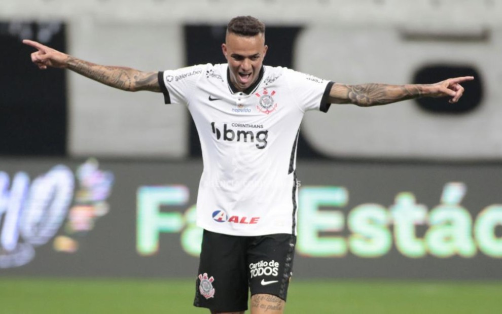 O jogador do Corinthians, Luan, comemora gol em campo, correndo com os braços abertos, vestido com o uniforme do time nas cores branco e preto