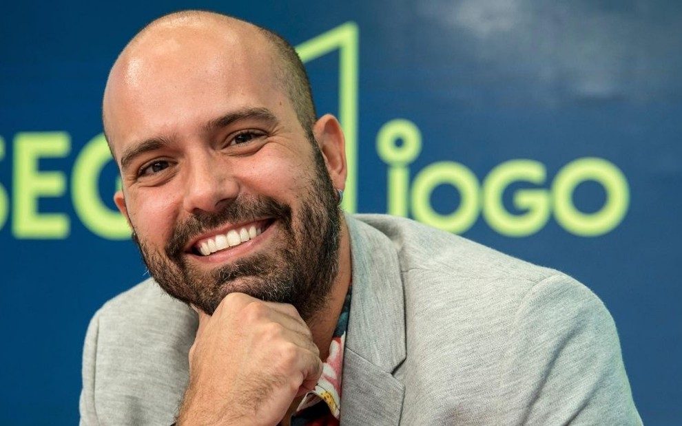 O jornalista Lucas Gutierrez em frente ao logo do programa Segue o Jogo, da Globo