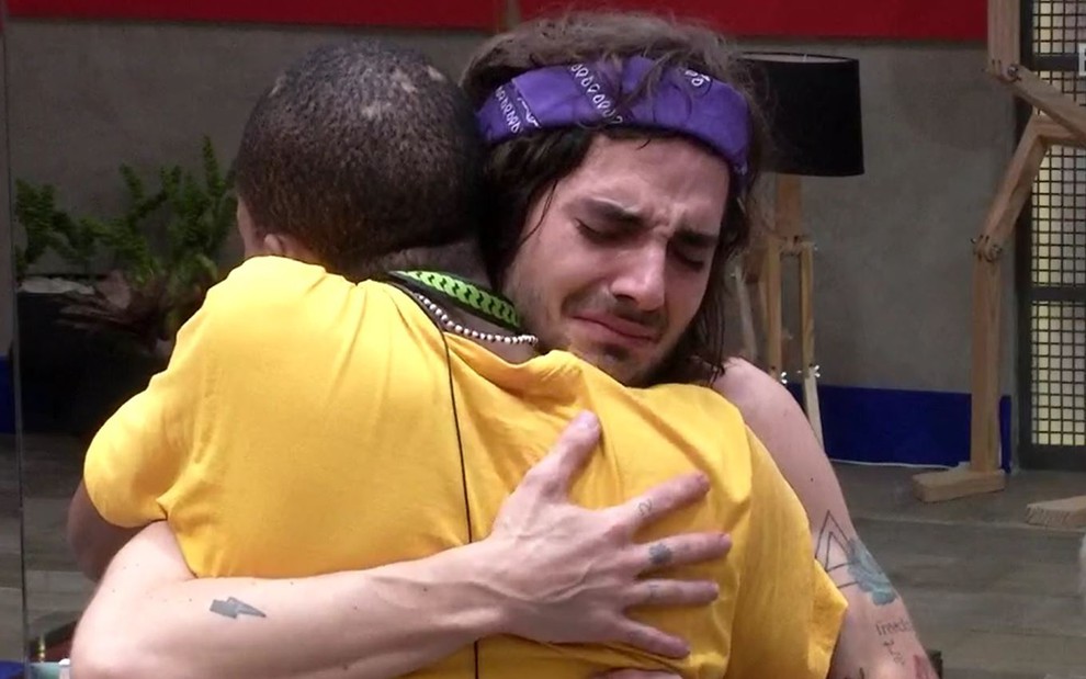 Fiuk está abraçado com Lucas, ele usa lenço roxo na cabeça; Lucas usa camiseta amarela