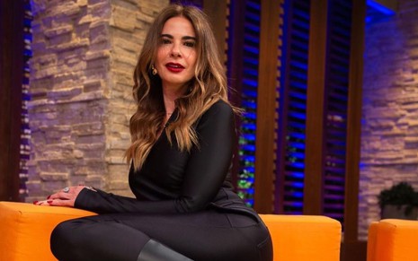 Luciana Gimenez de pernas cruzadas, sentada em um sofá laranja